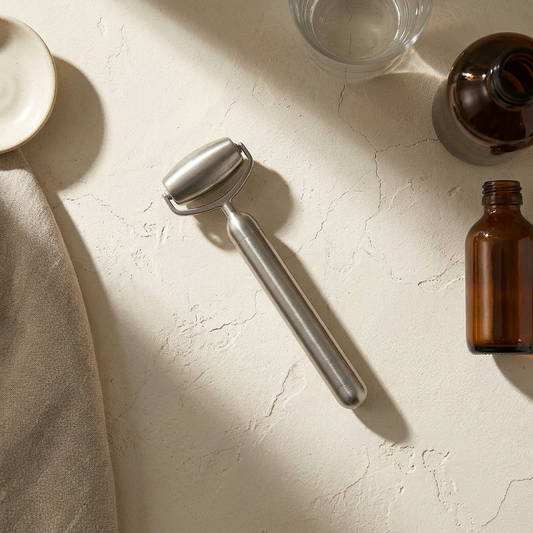 Lumi Weighted Contour Roller, solid stainless steel, on a bone plaster counter in window light